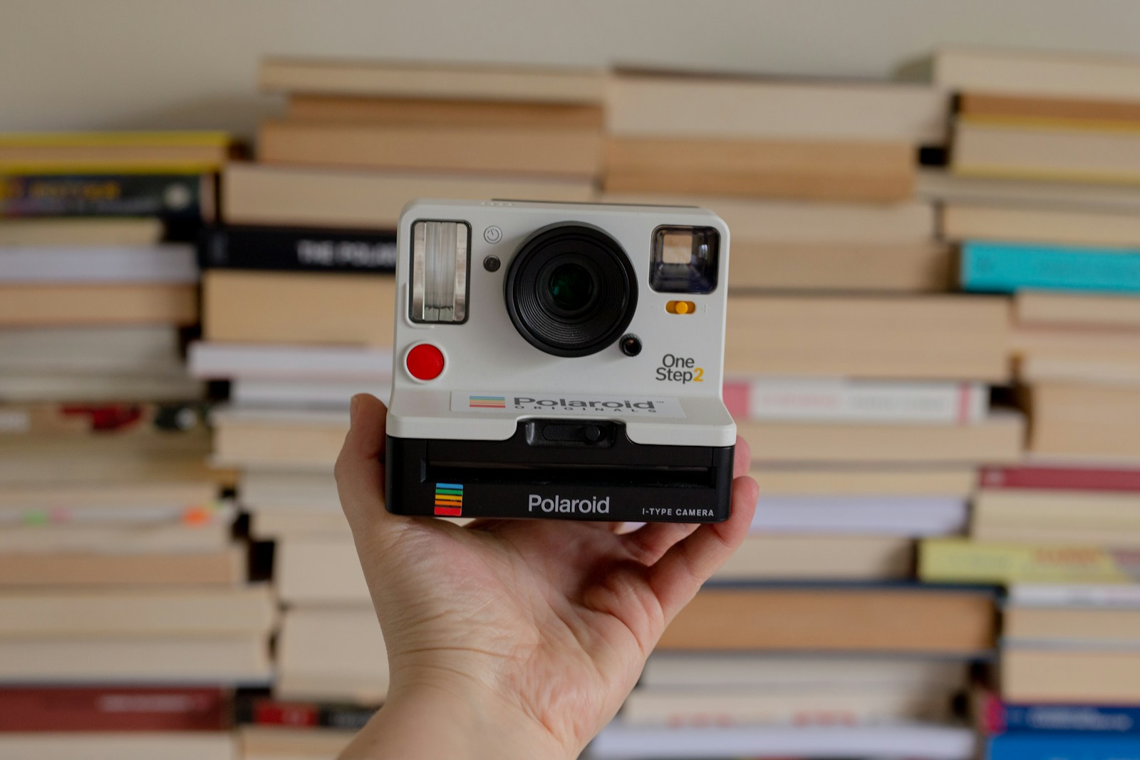 a person holding a polaroid camera in front of a stack of books