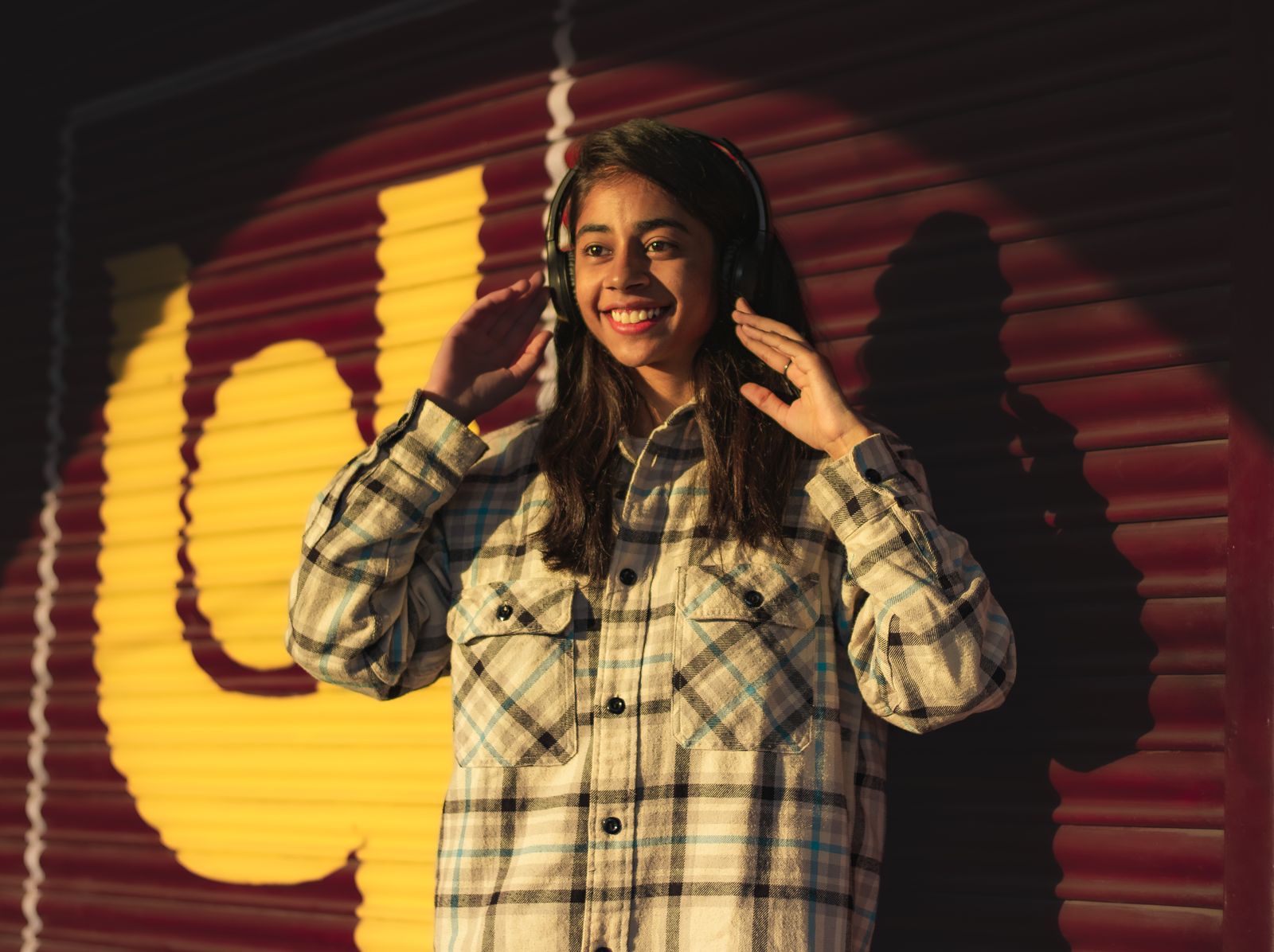 Smiling young woman with headphones outdoors in casual attire, enjoying music.